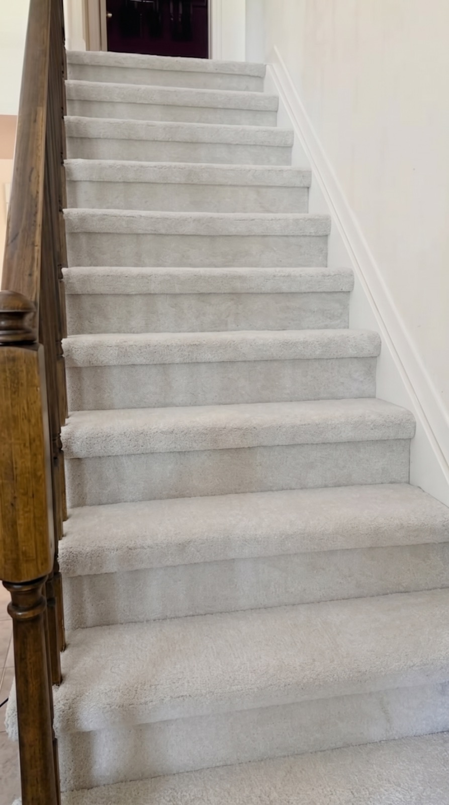 Staircase with plush light-gray carpet and a wood banister