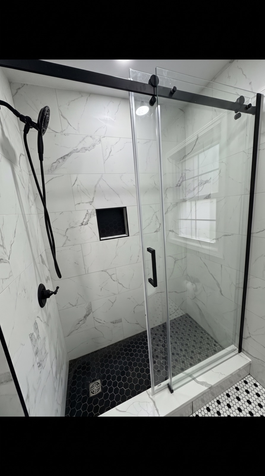 Marble tile shower with black-framed sliding glass door and hex mosaic floor