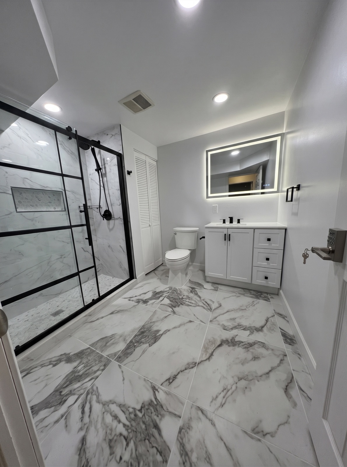 Bathroom with black-framed glass shower, marble-look floor, and lit mirror