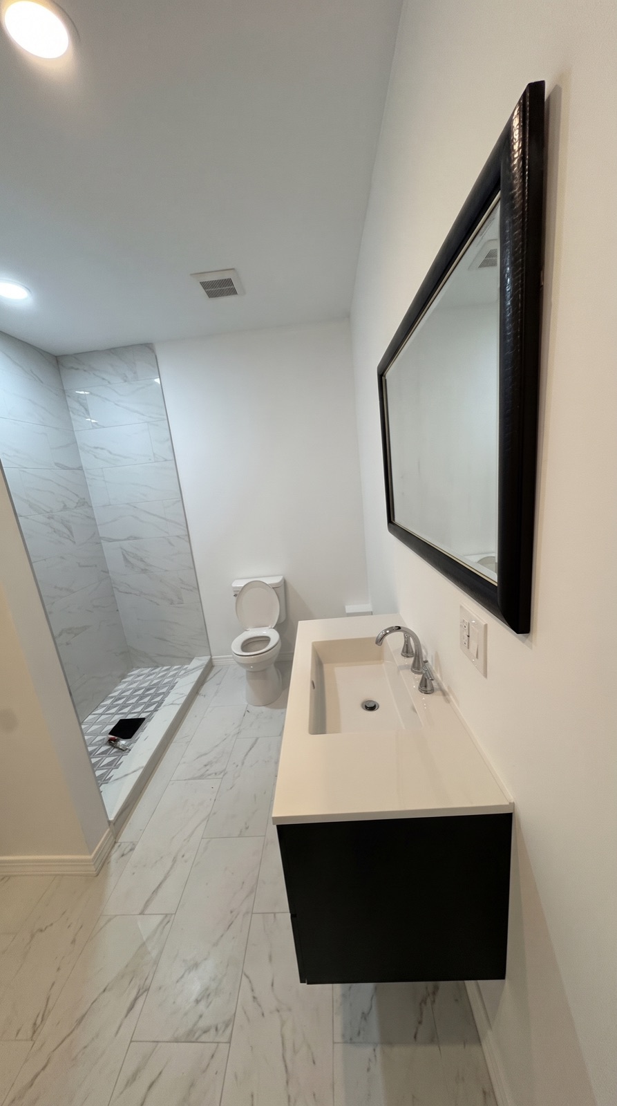 Bathroom remodel with marble-look tile shower, floating vanity, and large mirror