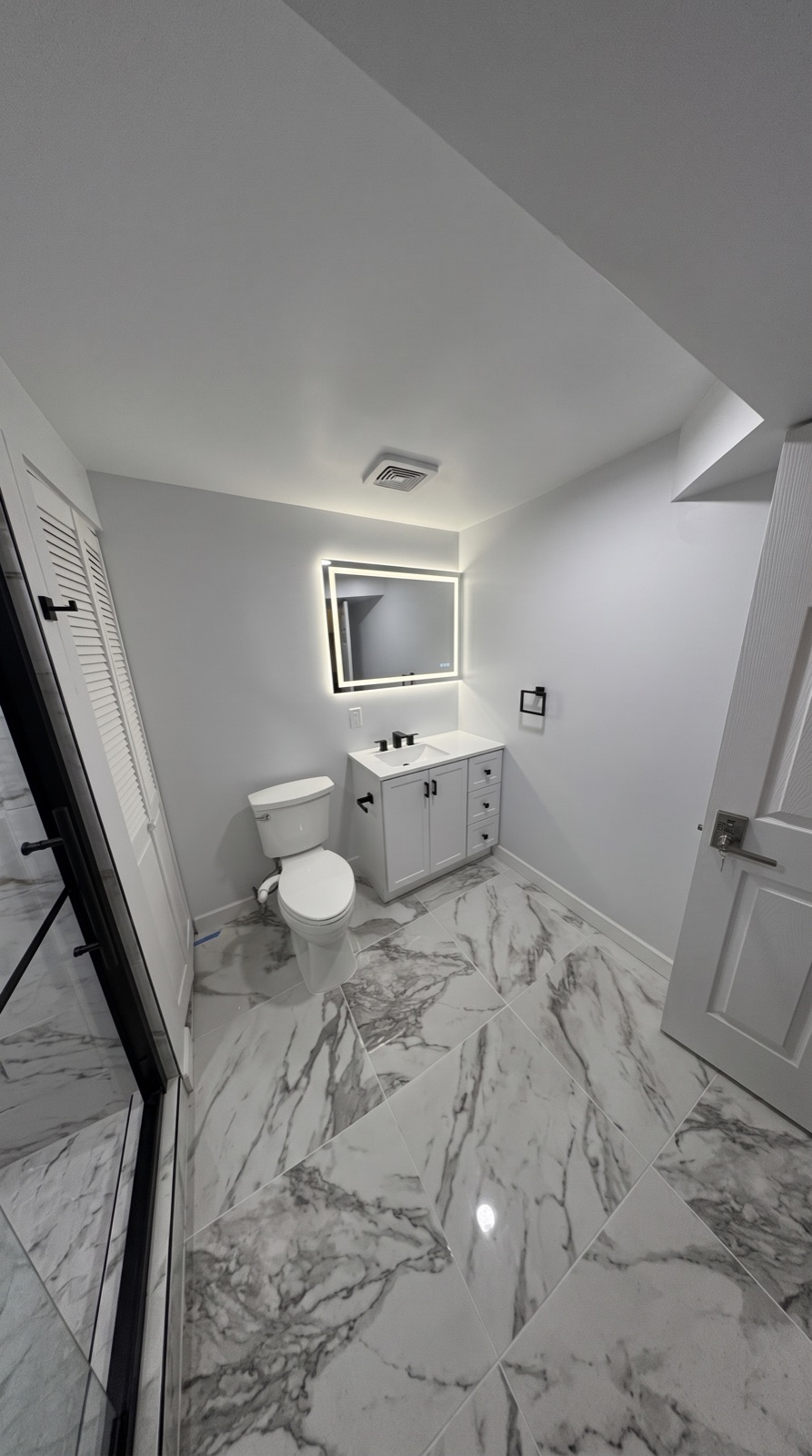 Bathroom with a white vanity, lit mirror, and marble-look tile floor