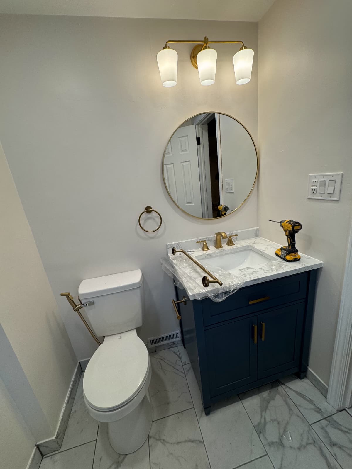 Powder room with navy vanity, marble counter, and gold sconce