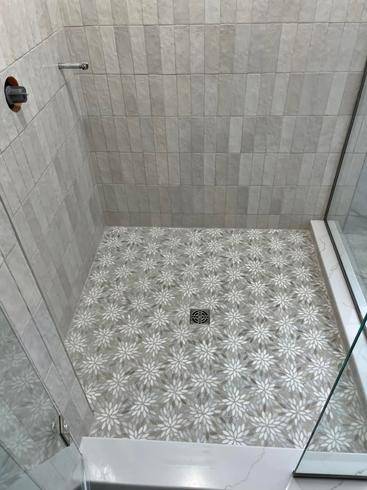 Vertical gray tile shower with floral mosaic floor